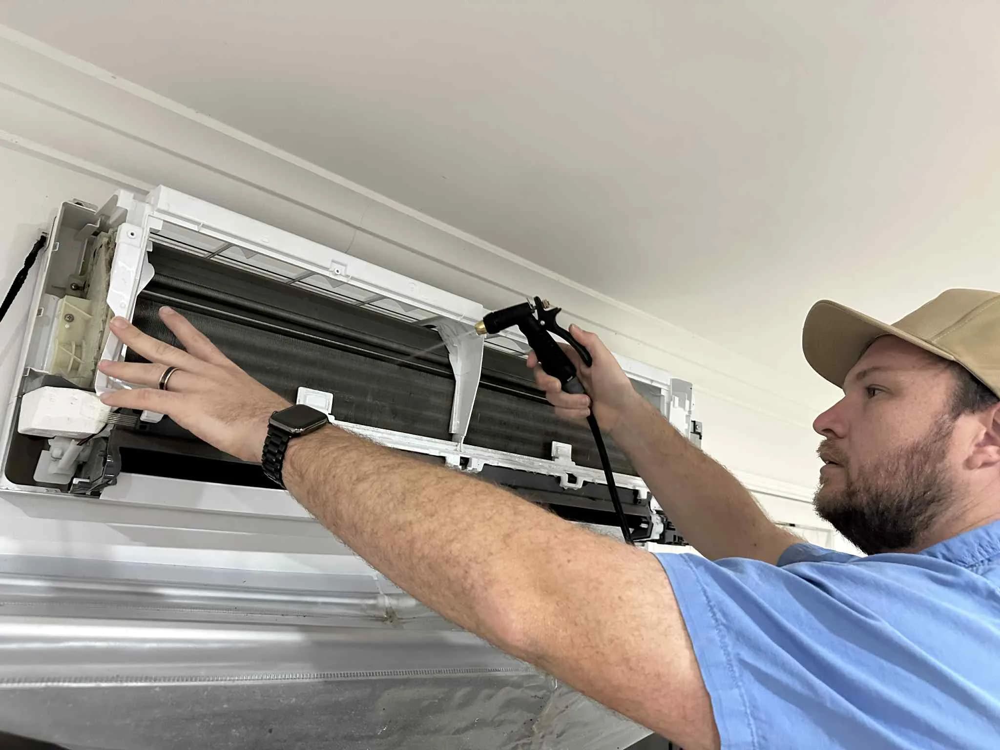 A Coola technician cleaning the coil of a wall-mounted split-system air conditioner in a Brisbane home