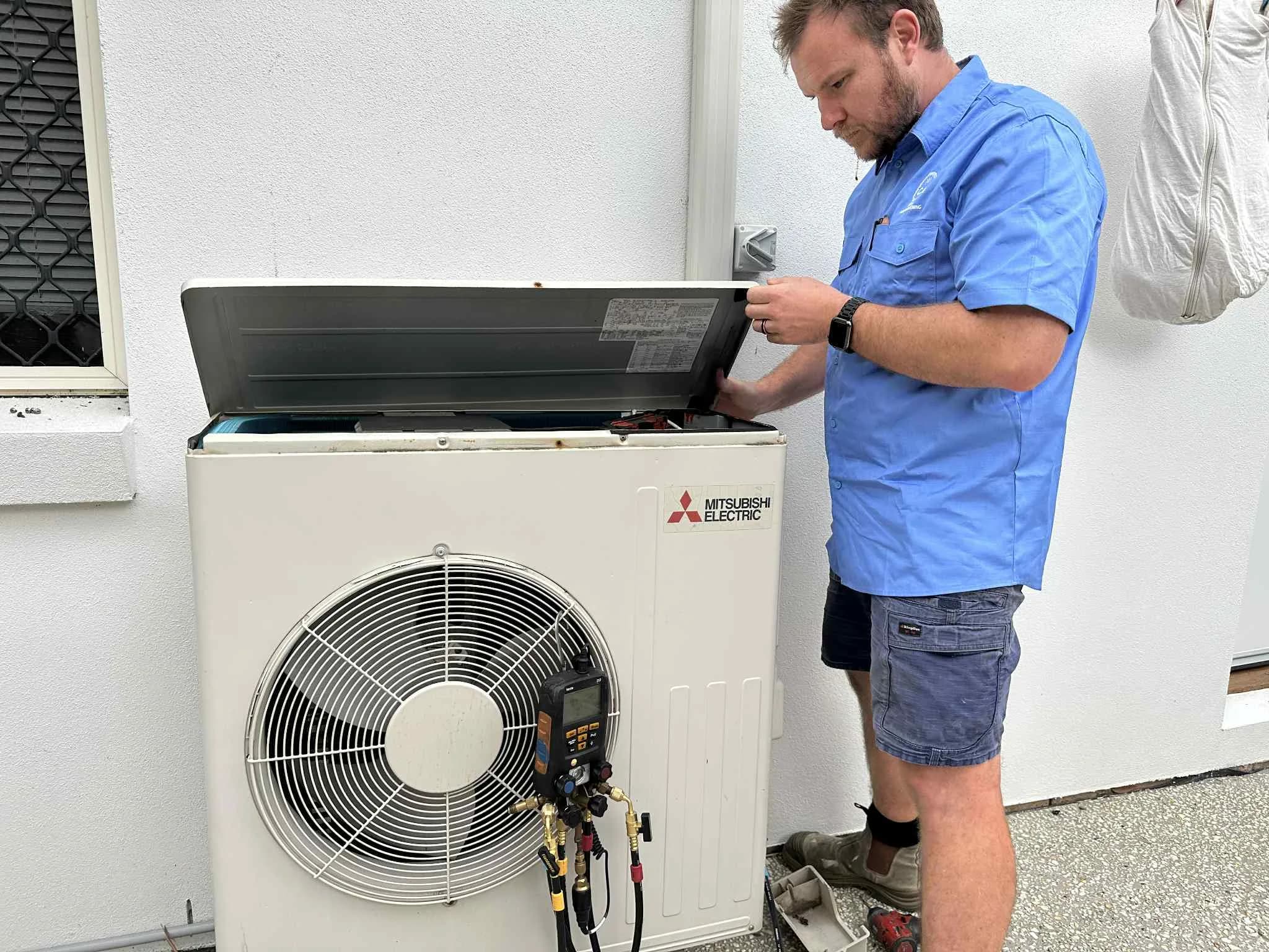 A Coola technician checking refrigerant pressures on a Mitsubishi Electric outdoor condenser at a Brisbane home
