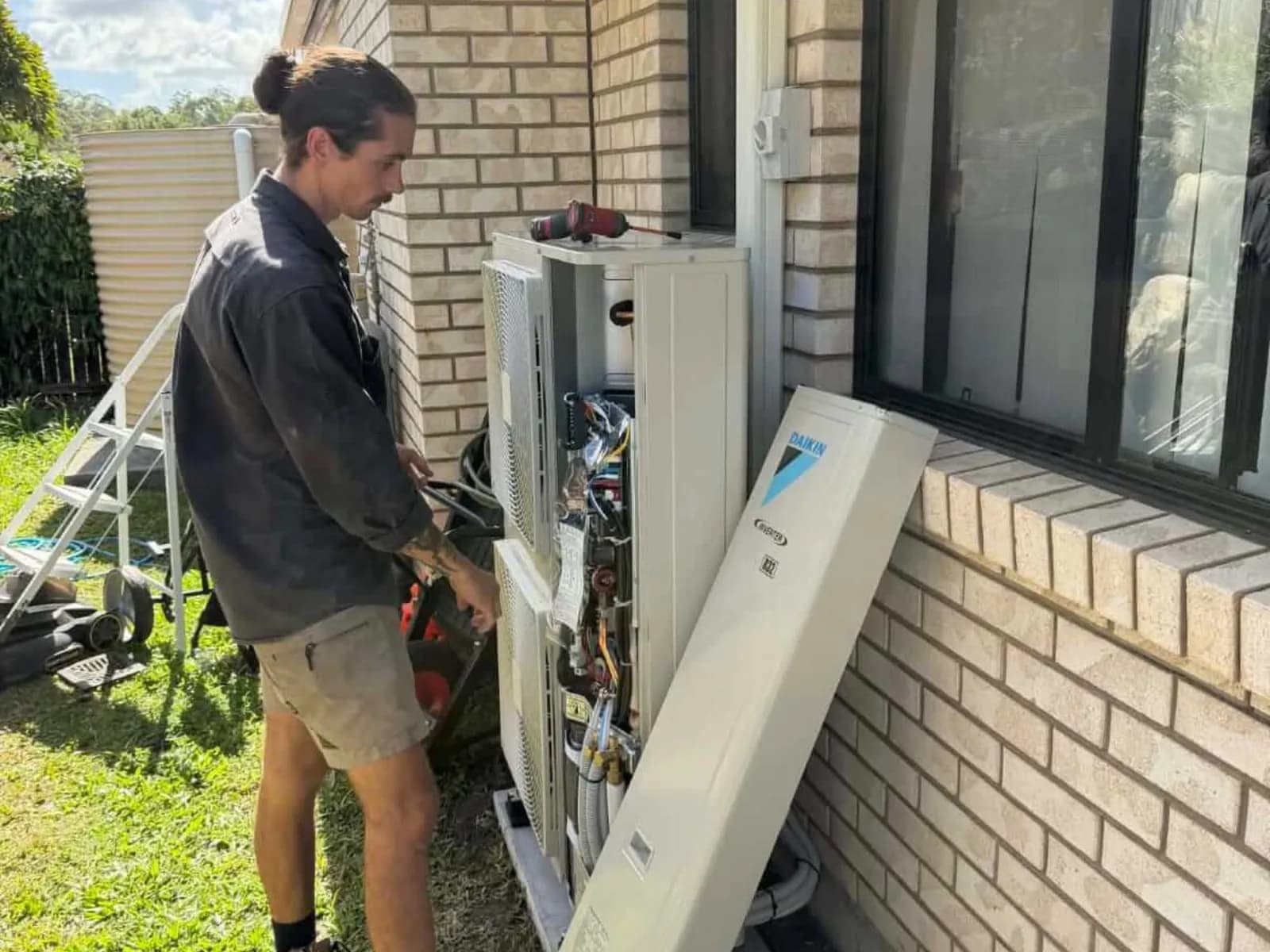 A Coola technician working on an outdoor air-conditioning unit at a brick Brisbane home