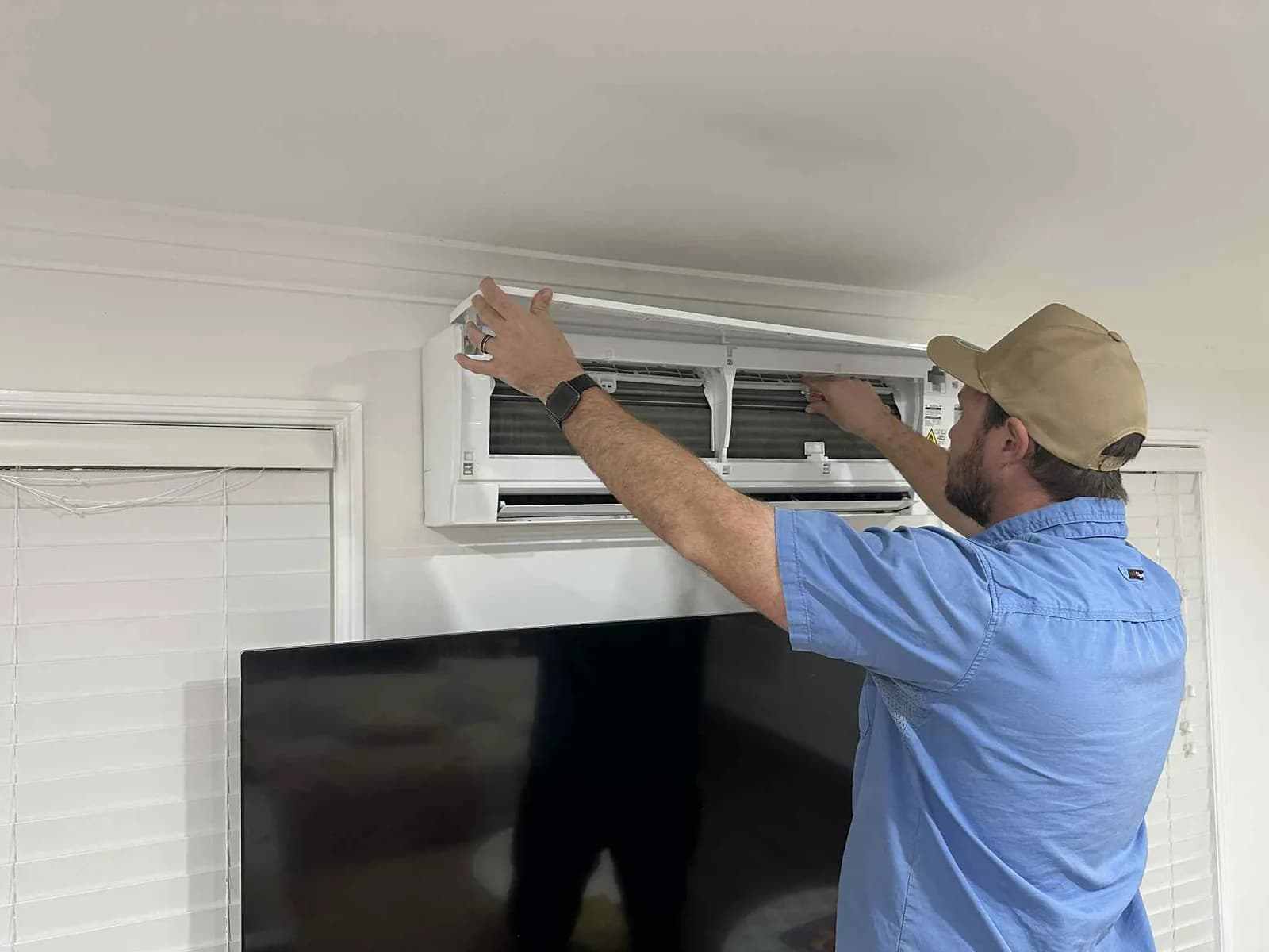 A Coola technician fitting a wall-mounted split-system head in a Brisbane living room