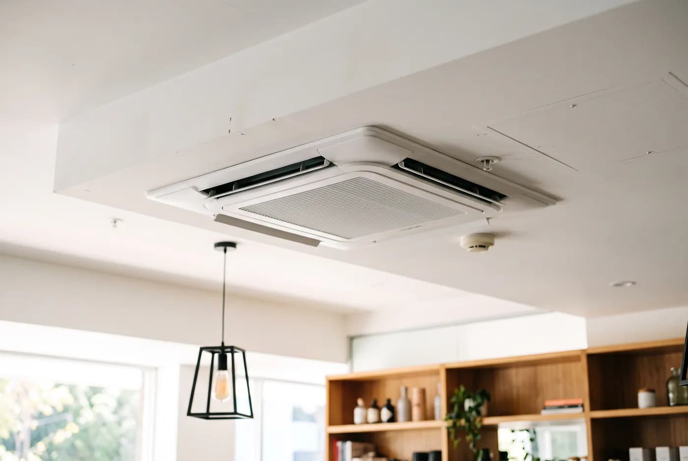 A white four-way ceiling cassette air conditioner set flush into a bright commercial ceiling